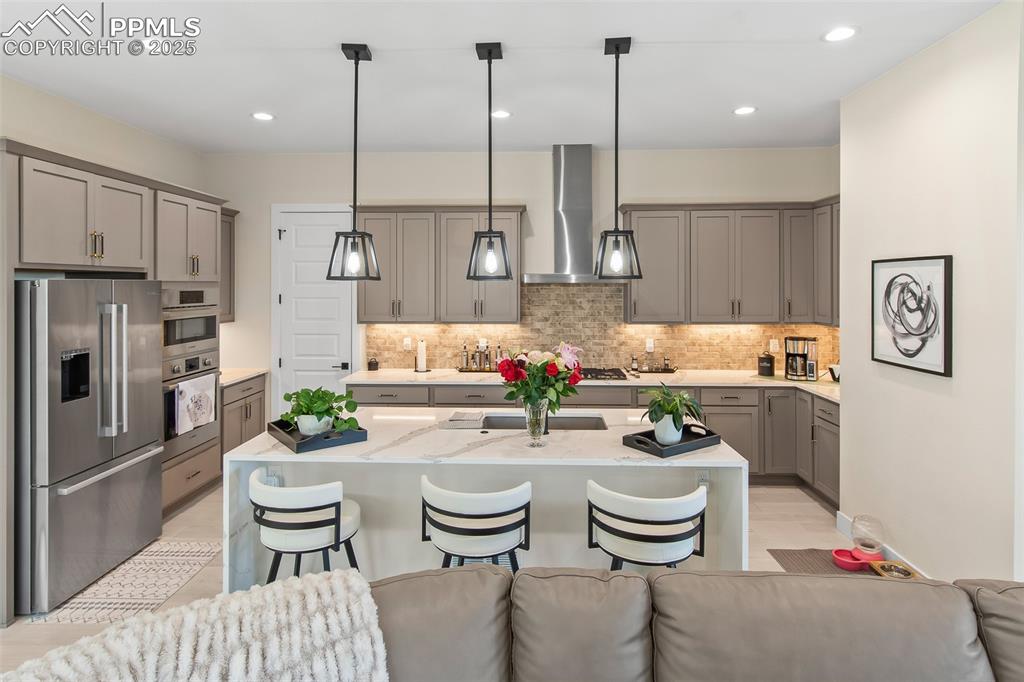 Image 20 of 48: Kitchen with gray cabinetry, stainless steel fridge, light stone counters,