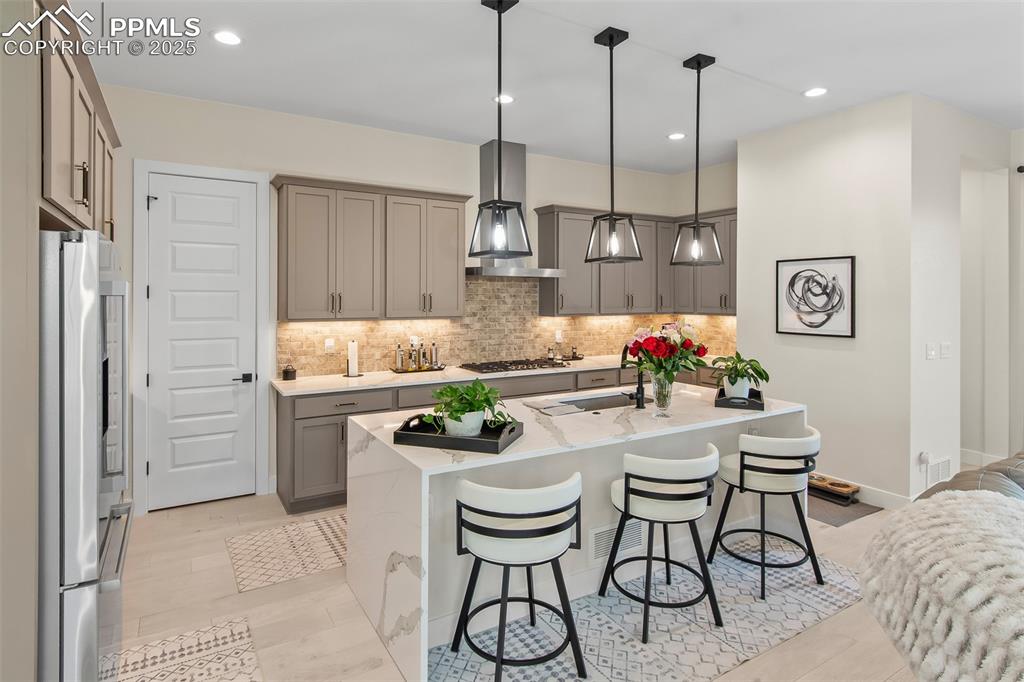 Image 21 of 48: Kitchen with gray cabinetry, a kitchen bar, light stone counters, a center