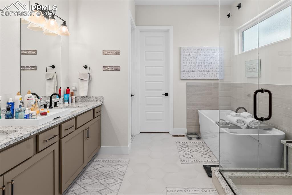 Image 34 of 48: Full bath with a soaking tub, double vanity, a shower stall, and light tile