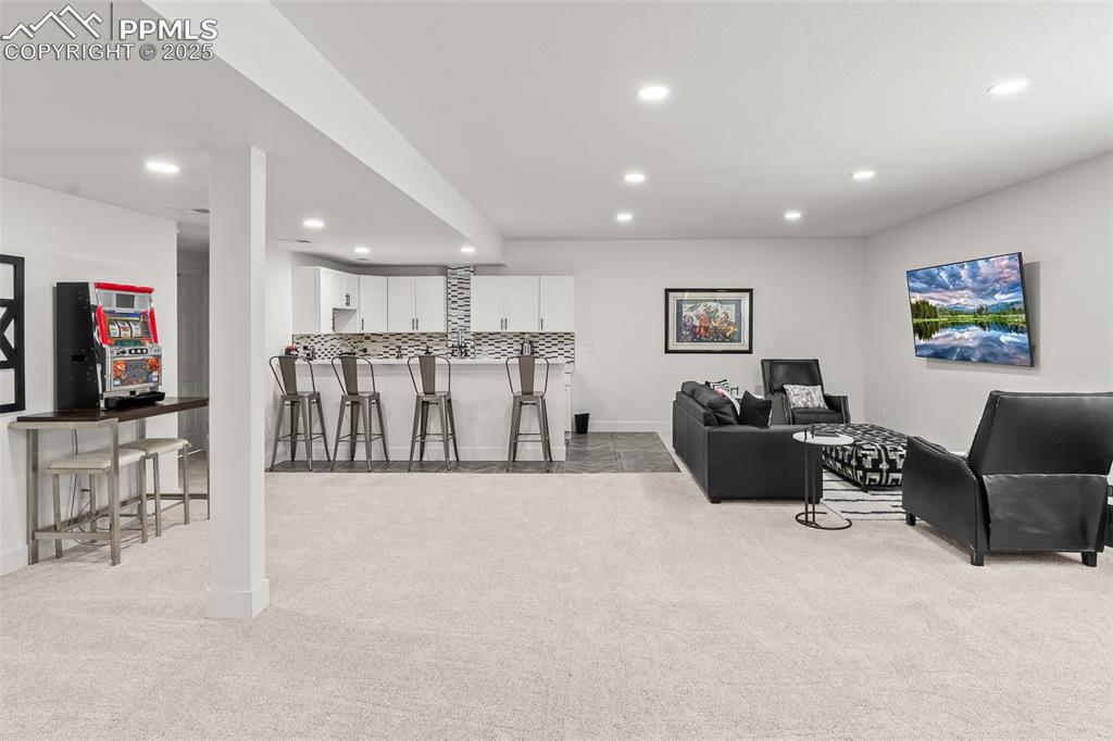 Image 38 of 48: Living room with light colored carpet, recessed lighting, and bar