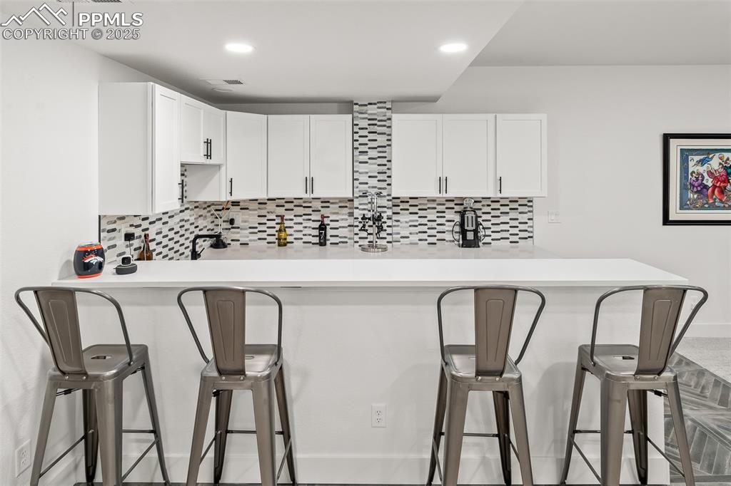 Image 40 of 48: Kitchen featuring a breakfast bar area, tasteful backsplash, white cabinets