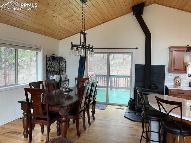 Image 20 of 39: Dining room with lofted ceiling, a wood stove, light wood-style floors, a c