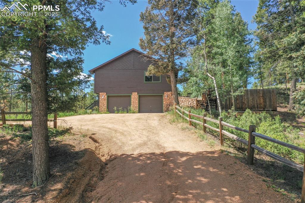Image 5 of 39: View of side of property with dirt driveway and an attached garage