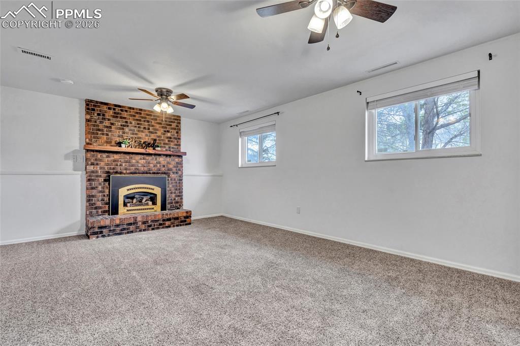 Image 26 of 31: Family room on lower level with gas fireplace, carpet, ceiling fans, and up
