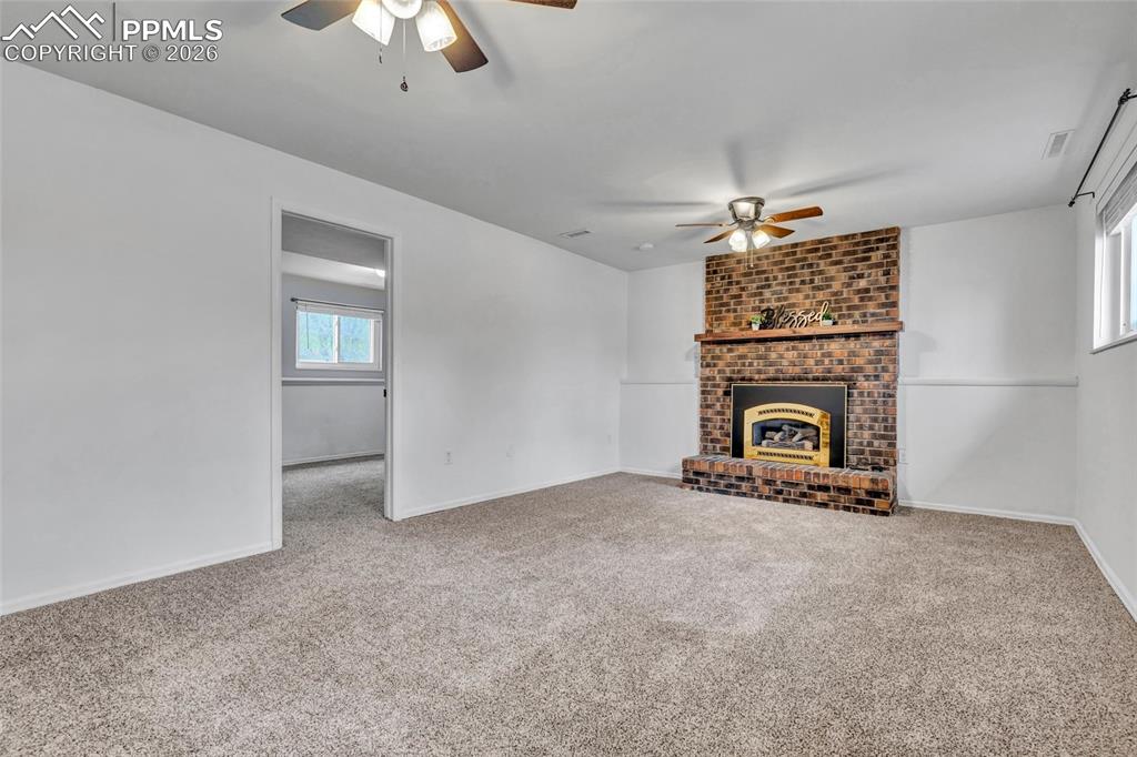 Image 27 of 31: Family room on lower level with gas fireplace, carpet, ceiling fans, and up