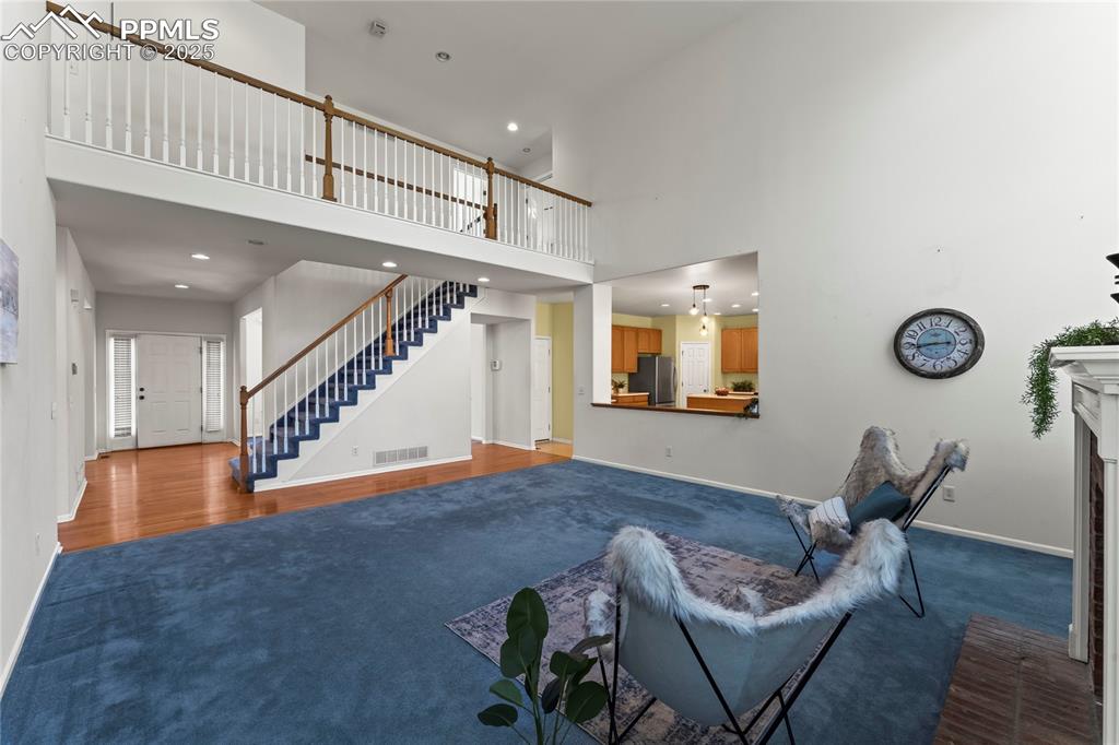 Image 16 of 49: Living room with a towering ceiling, a fireplace, dark carpet, stairway, an