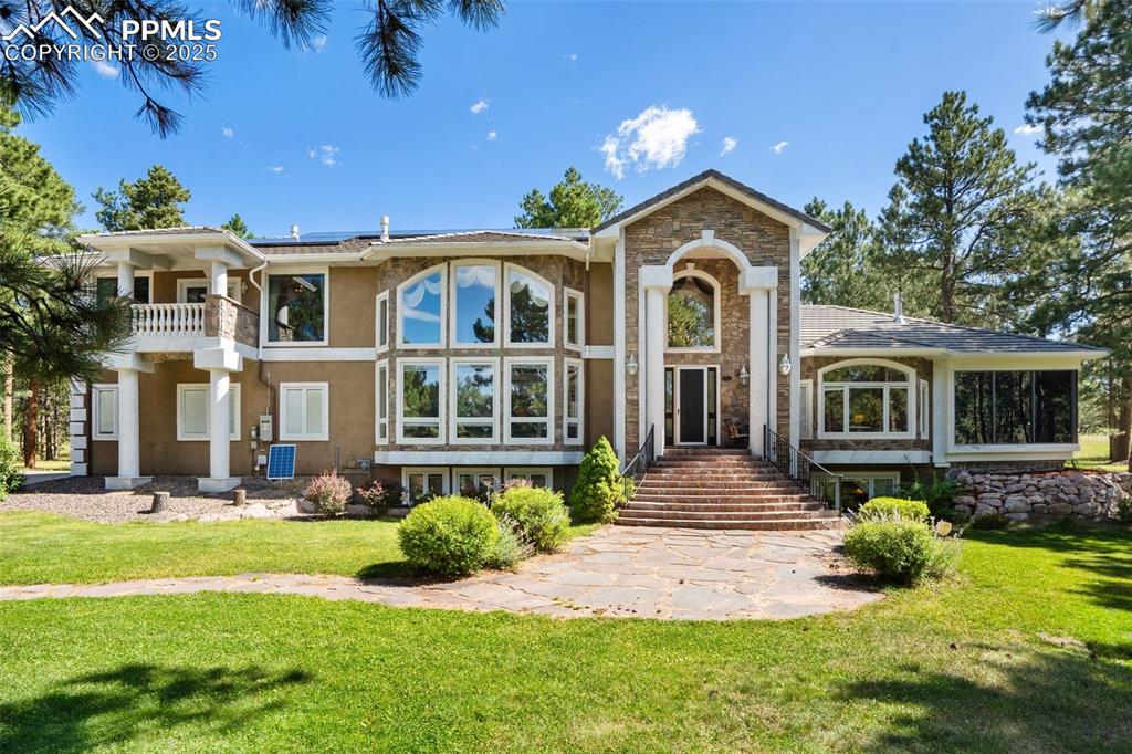 Caption: View of front facade featuring solar panels, a front yard, stucco siding, stone siding, and a balcon