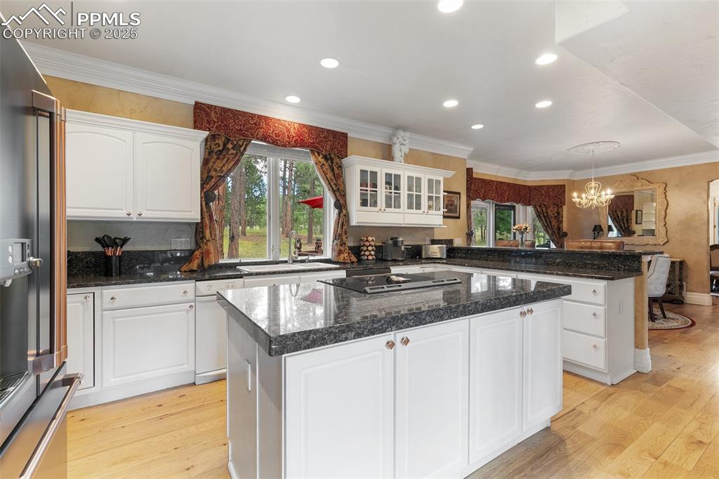 Image 14 of 50: Kitchen with a peninsula, a chandelier, black electric stovetop, light wood