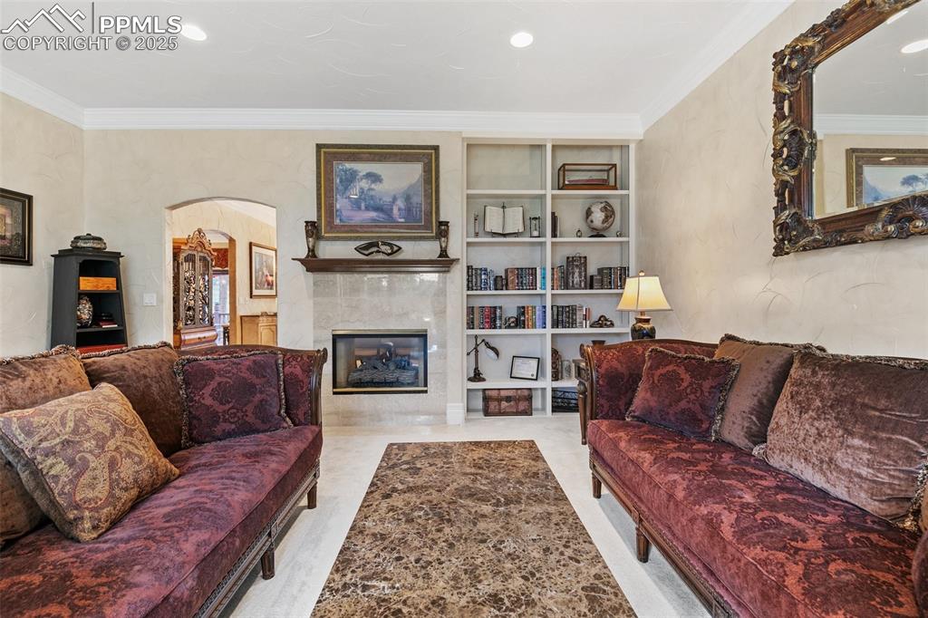Image 18 of 50: Living room with arched walkways, ornamental molding, a tile fireplace, bui