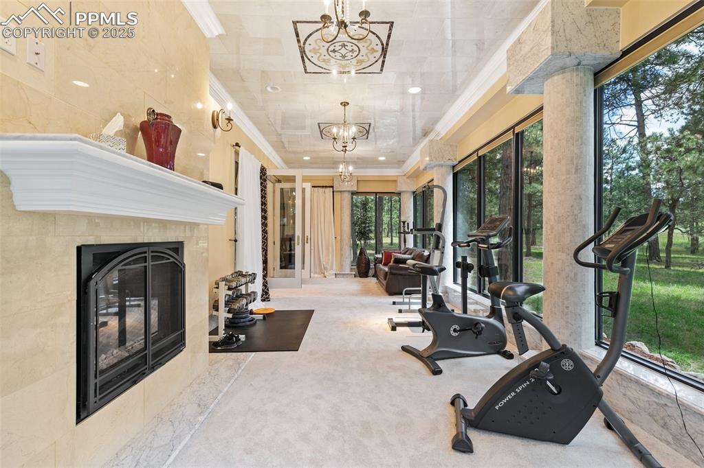 Image 20 of 50: Exercise area featuring a chandelier, crown molding, a fireplace, and carpe