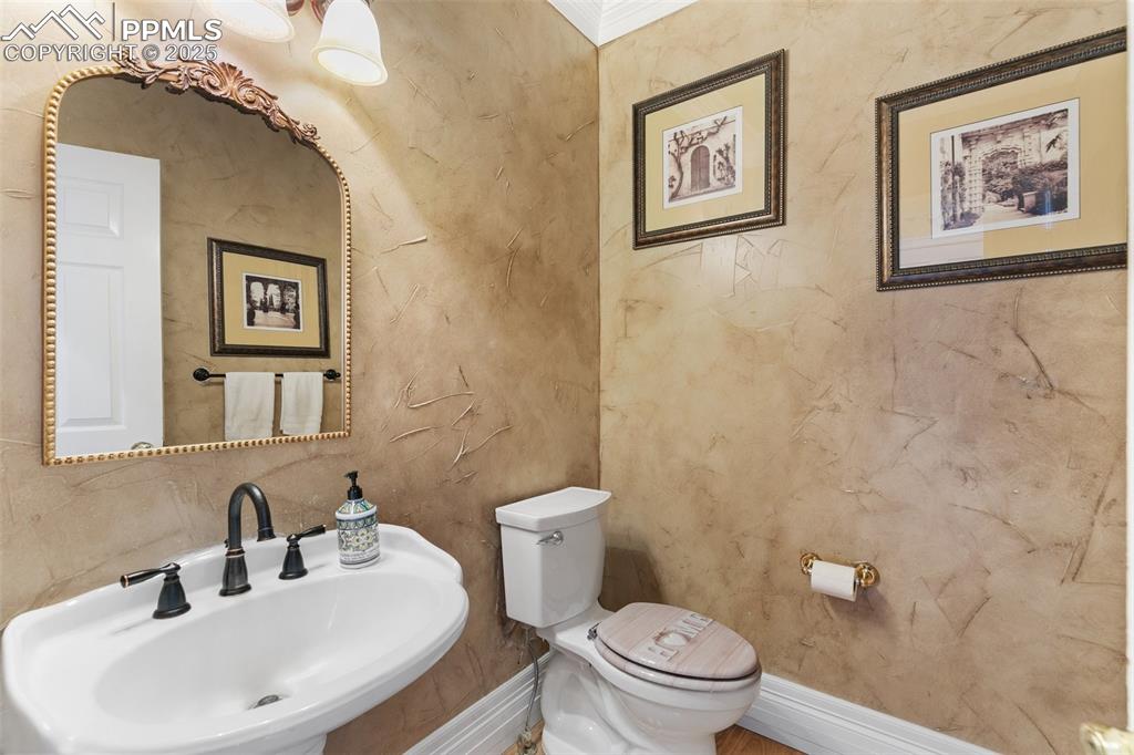 Image 21 of 50: Half bathroom with a sink, toilet, and baseboards