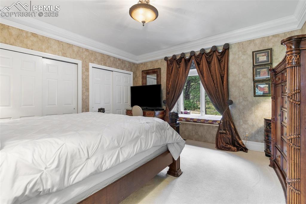 Image 26 of 50: Carpeted bedroom featuring two closets, crown molding, wallpapered walls, a