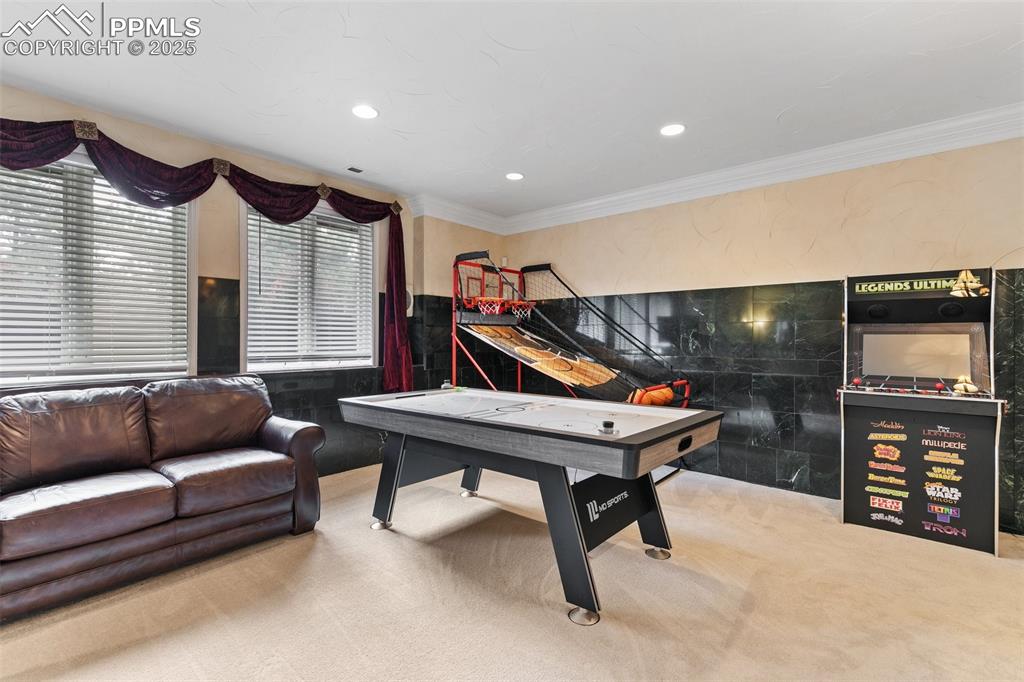 Image 39 of 50: Game room with carpet flooring, crown molding, tile walls, and recessed lig