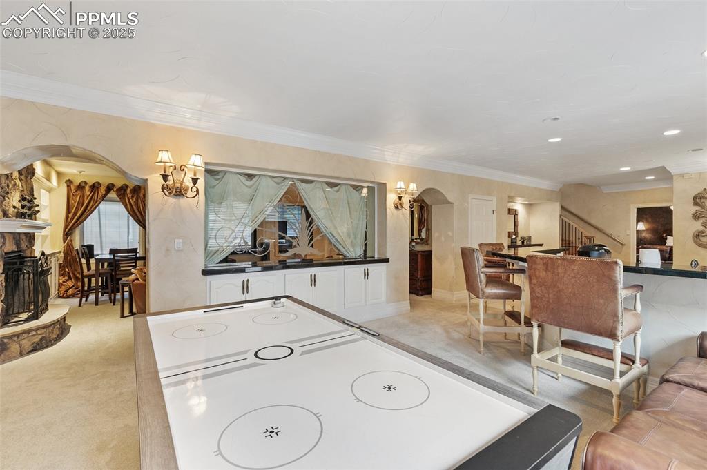 Image 41 of 50: Game room with arched walkways, a chandelier, crown molding, a fireplace, a