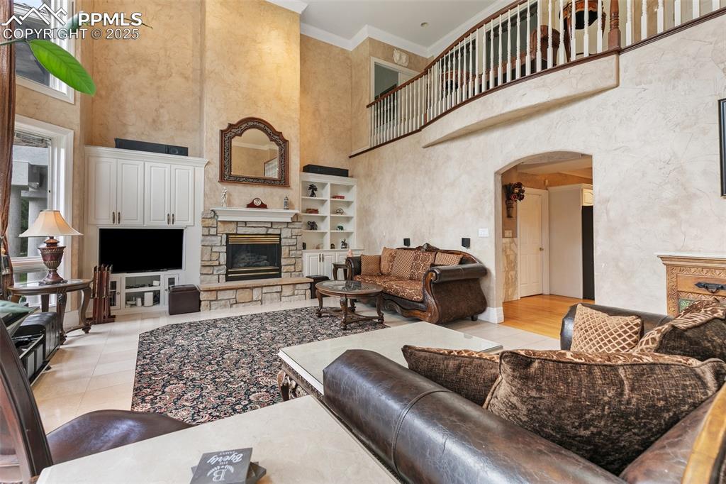 Image 7 of 50: Living area with a stone fireplace, arched walkways, a high ceiling, orname