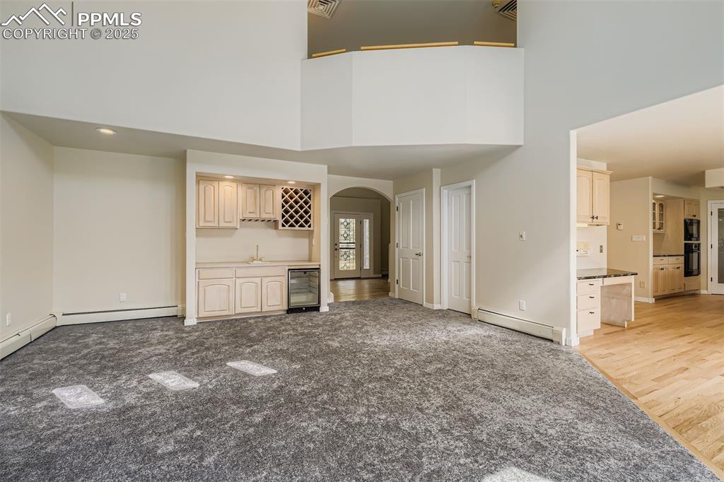 Image 5 of 35: Unfurnished living room with arched walkways, baseboard heating, bar with s