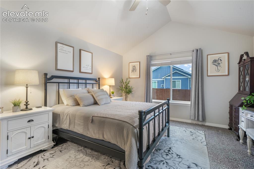 Image 14 of 50: Vaulted ceiling, ceiling fan, carpeting, window with curtains, and gray wal