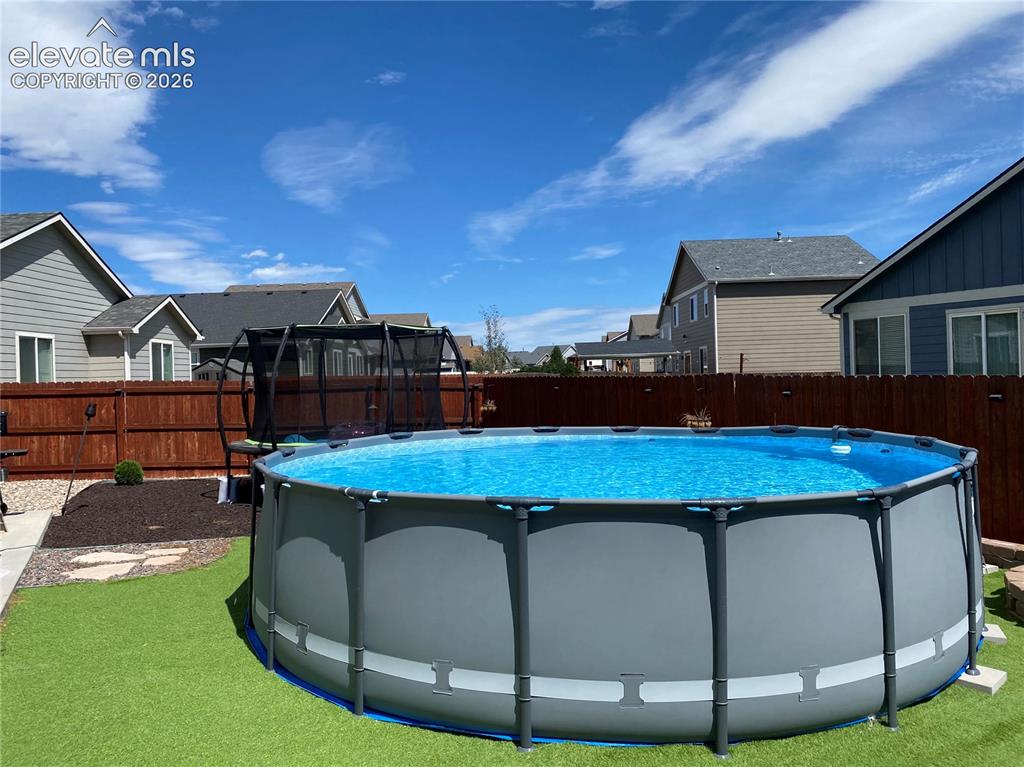 Image 37 of 50: Backyard featuring an above-ground pool, artificial turf, wood fencing, and