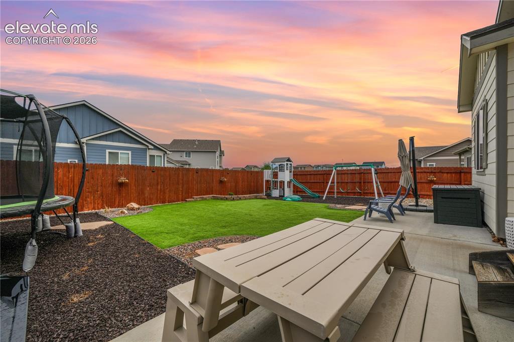 Image 38 of 50: Private backyard featuring a concrete patio, wood fence, and artificial tur