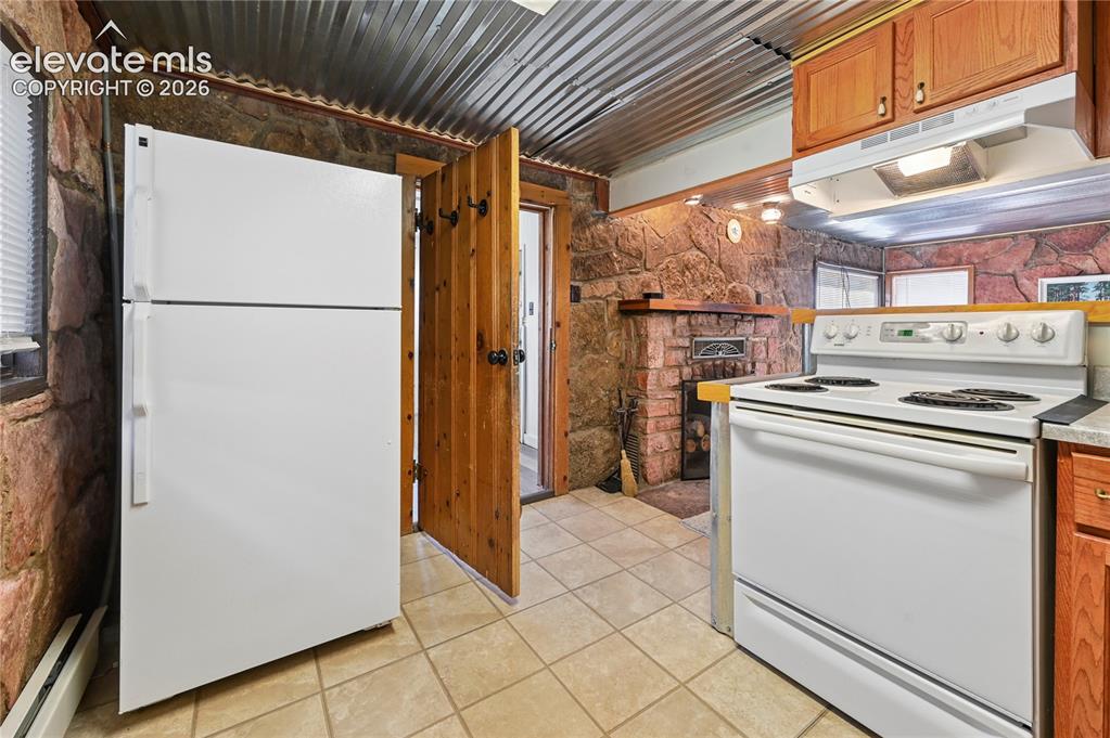 Image 23 of 45: Basement kitchenette with electric stove, fridge, and stone walls that add