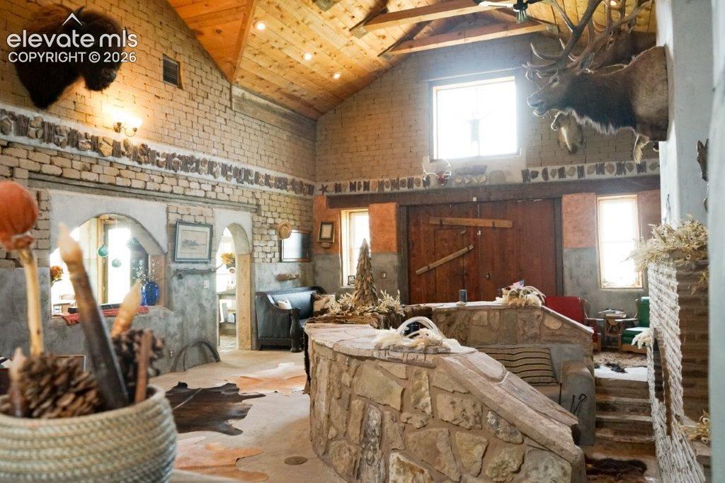 Image 16 of 50: Vaulted wood-paneled ceiling with exposed beams, adobe brick walls, and sto
