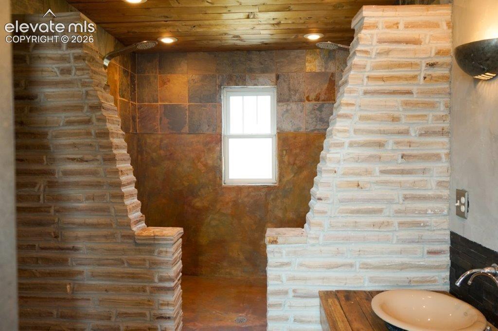 Image 45 of 50: Stone-clad shower enclosure featuring a fixed window and a wood-finish ceil
