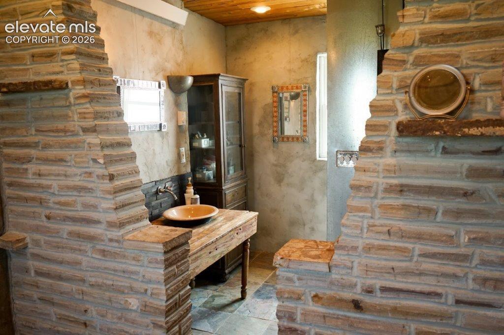 Image 46 of 50: Stone-clad interior walls featuring a wooden vanity with a vessel sink