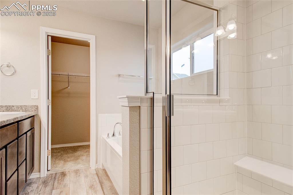 Image 16 of 24: Full bath with vanity, a bath, a spacious closet, light wood-style floors, 
