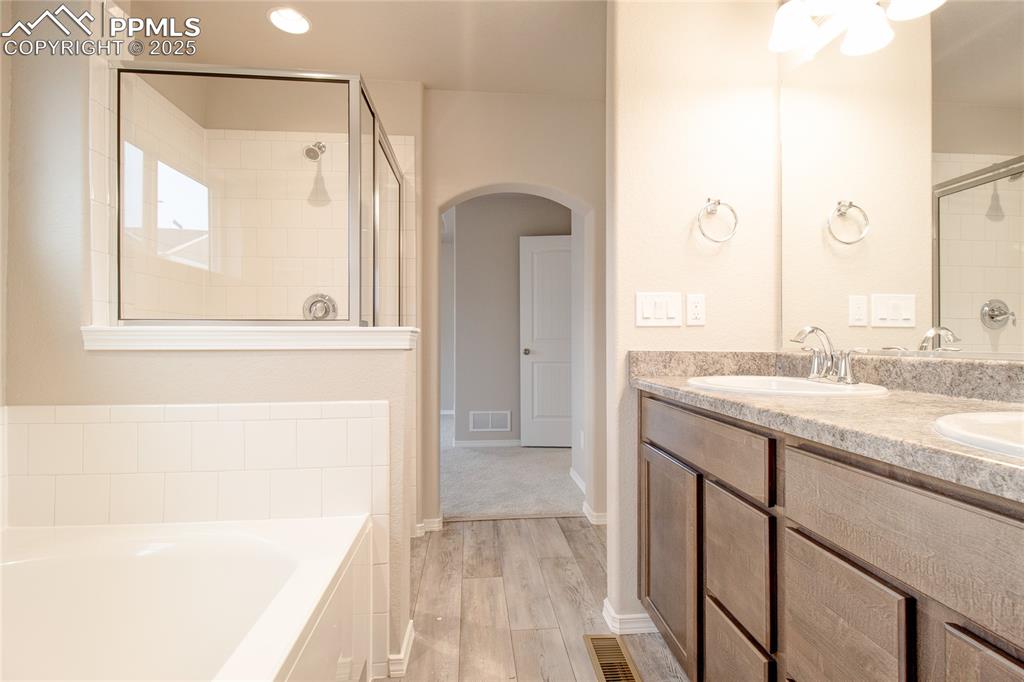 Image 21 of 24: Full bath featuring a bath, double vanity, a stall shower, and light wood-s