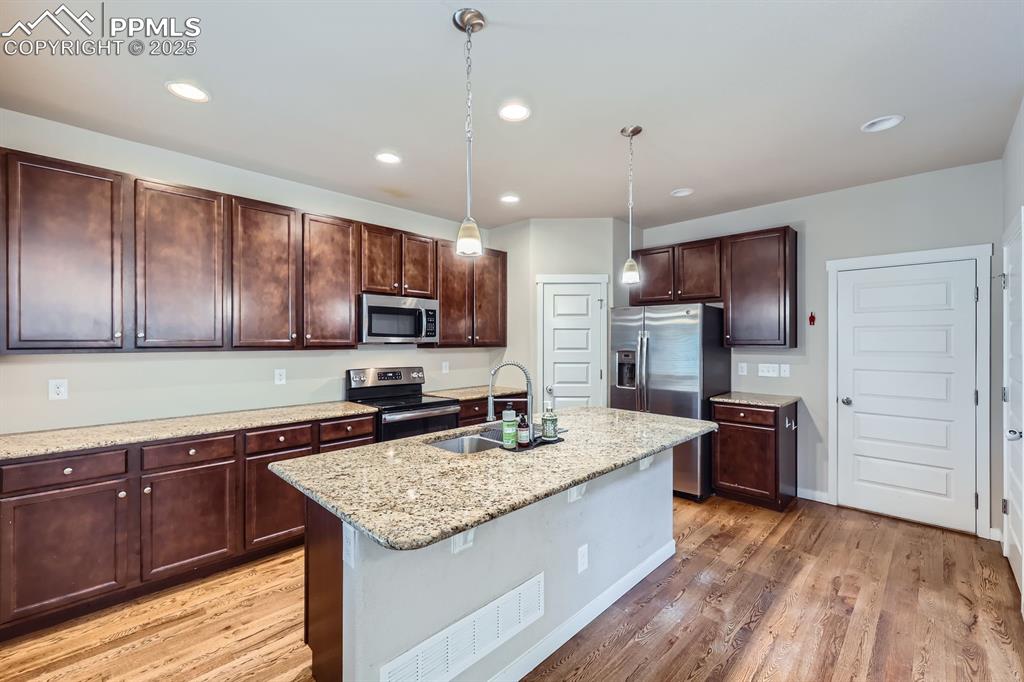 Image 10 of 31: Kitchen featuring dark brown cabinets, hanging light fixtures, stainless st