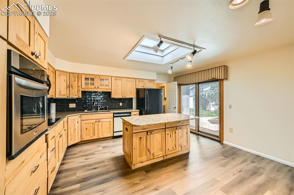 Image 10 of 29: Kitchen featuring black appliances, a skylight, light brown cabinets, a cen