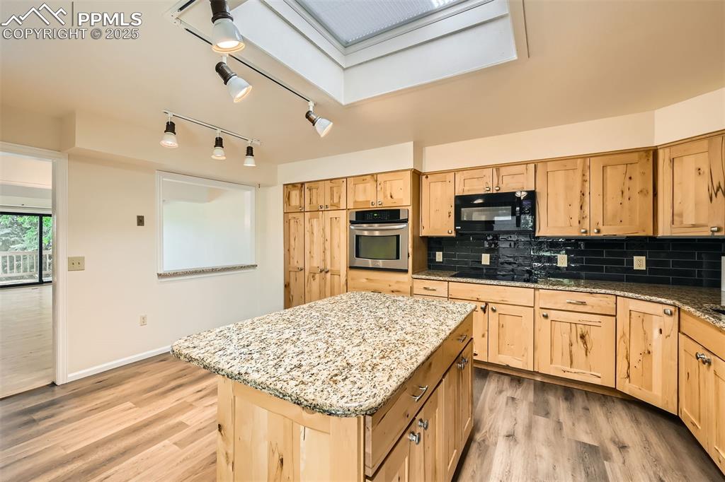 Image 11 of 29: Kitchen with black appliances, light brown cabinetry, light wood-style floo