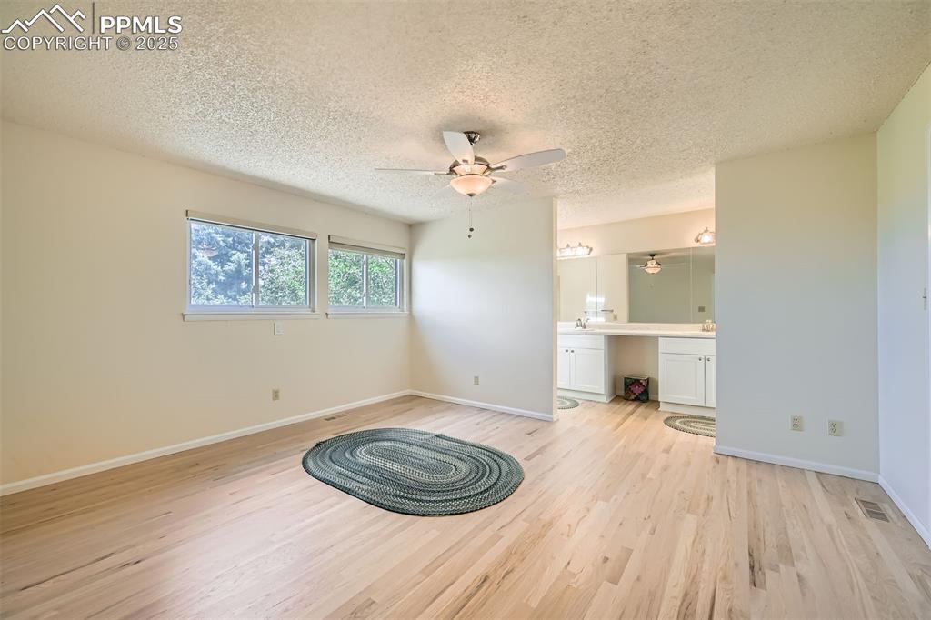 Image 16 of 29: Primary bedroom with light wood-style floors, a textured ceiling, ensuite b