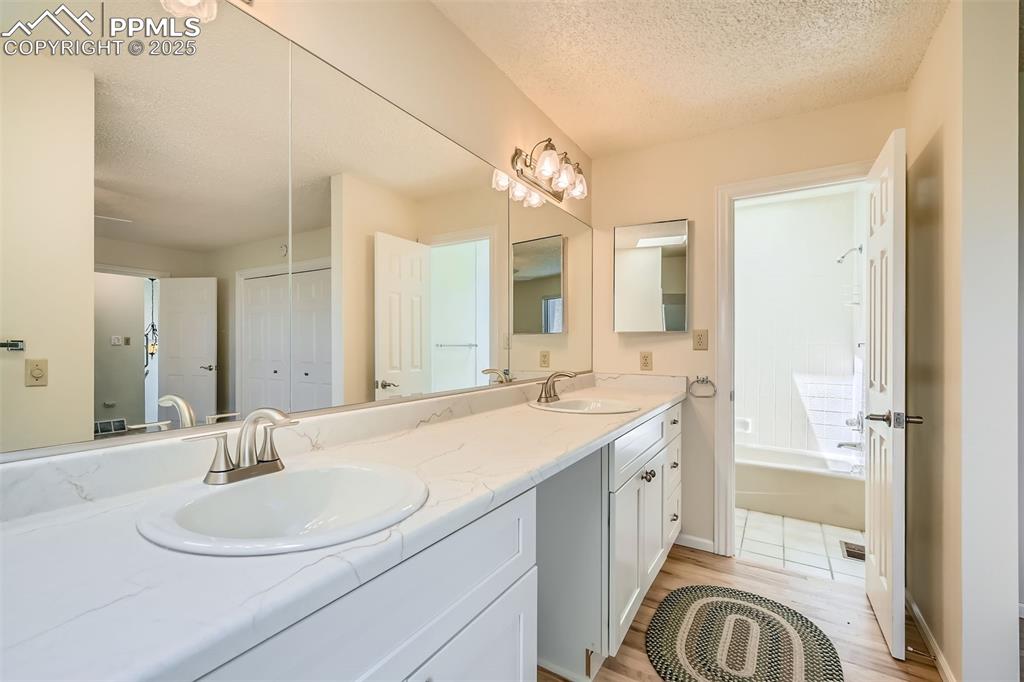 Image 20 of 29: Bathroom featuring double vanity, wood finished floors, a textured ceiling,