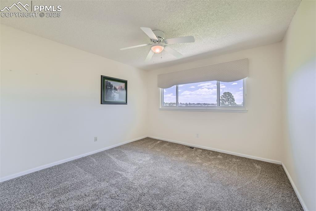 Image 21 of 29: Carpeted bedroom with a textured ceiling and ceiling fan