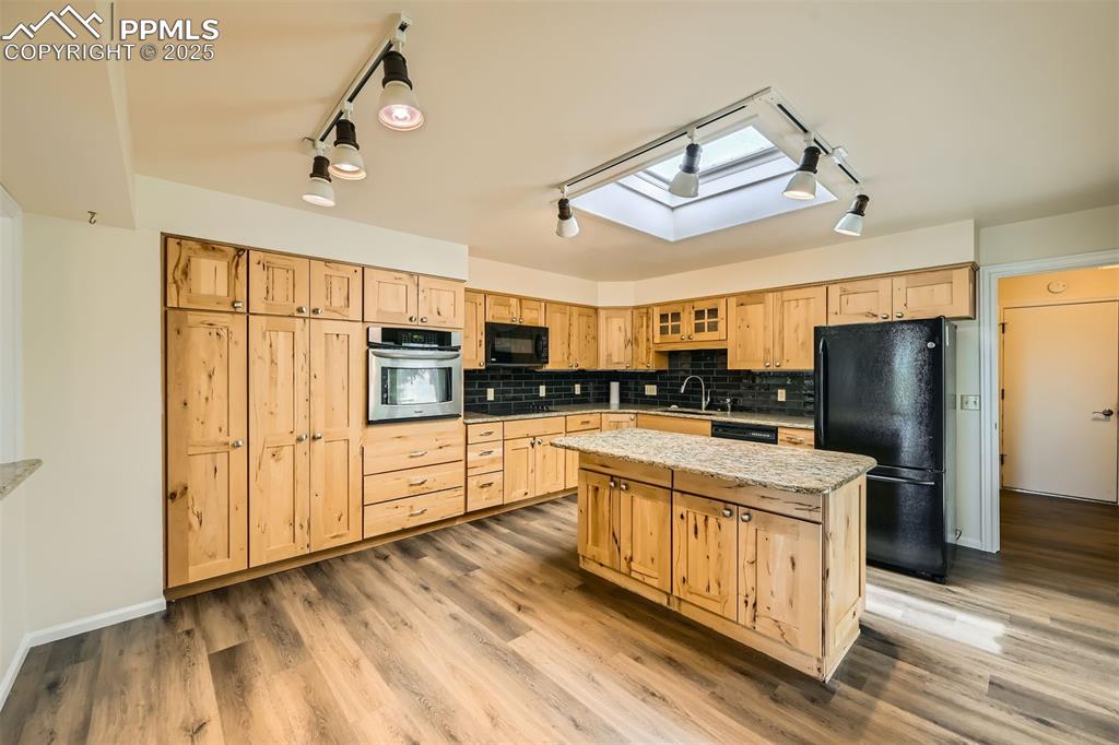Image 9 of 29: Kitchen featuring black appliances, a skylight, light brown cabinetry, and