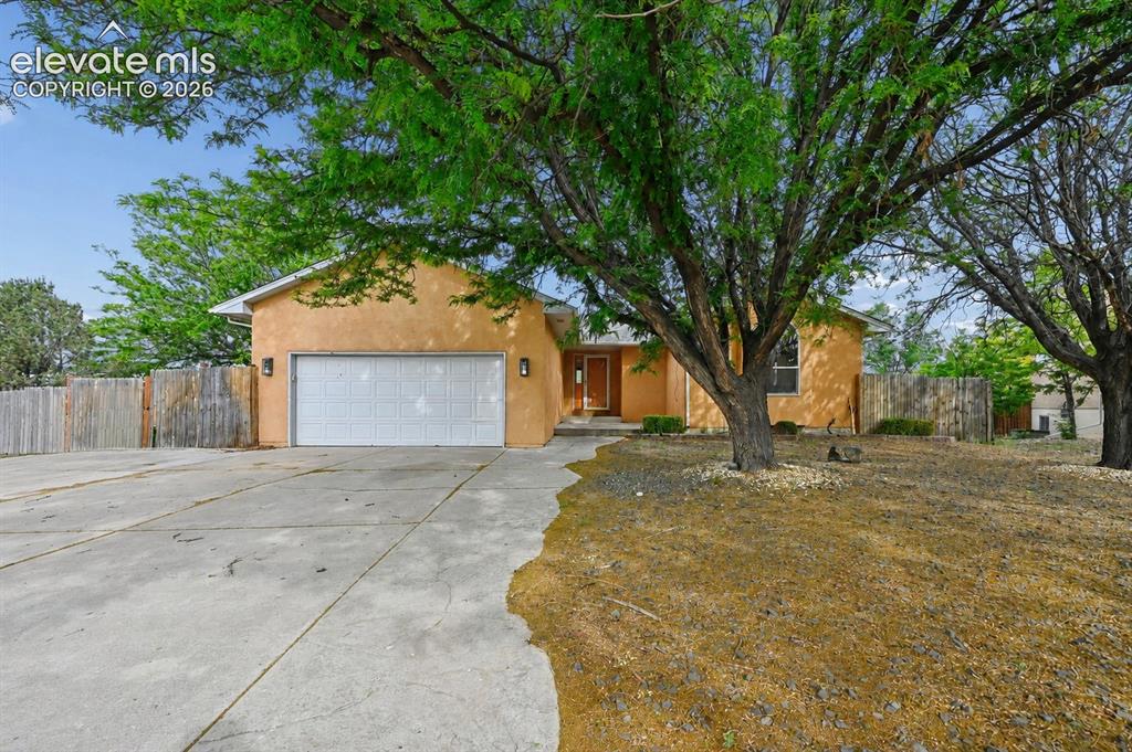 Image 1 of 32: Stucco exterior with an attached garage, paved driveway, and mature landsca