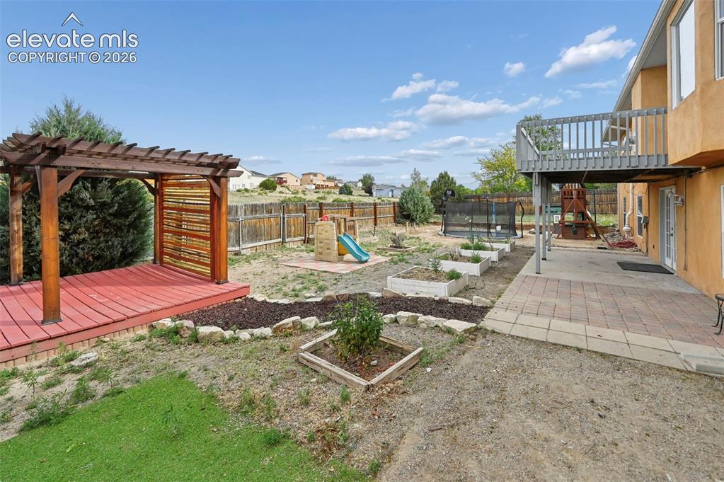 Image 19 of 32: Expansive backyard featuring a wood pergola with a red-stained deck, multip