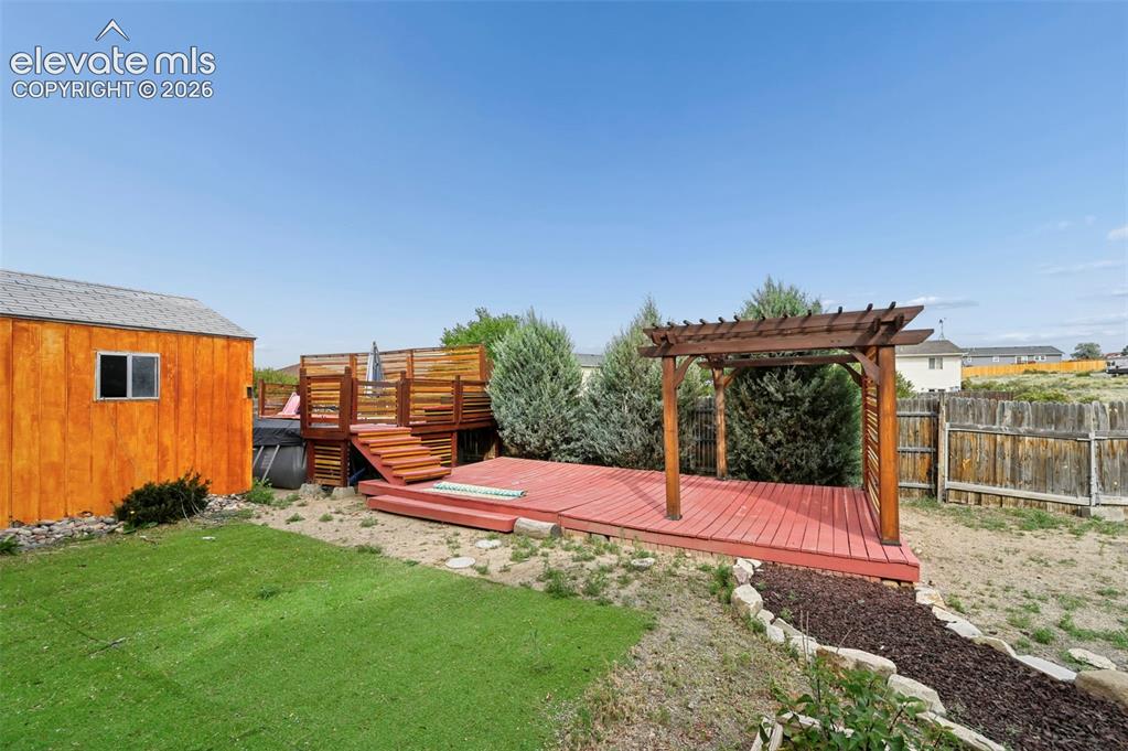 Image 22 of 32: Expansive backyard featuring a red-stained deck with a pergola, a multi-lev