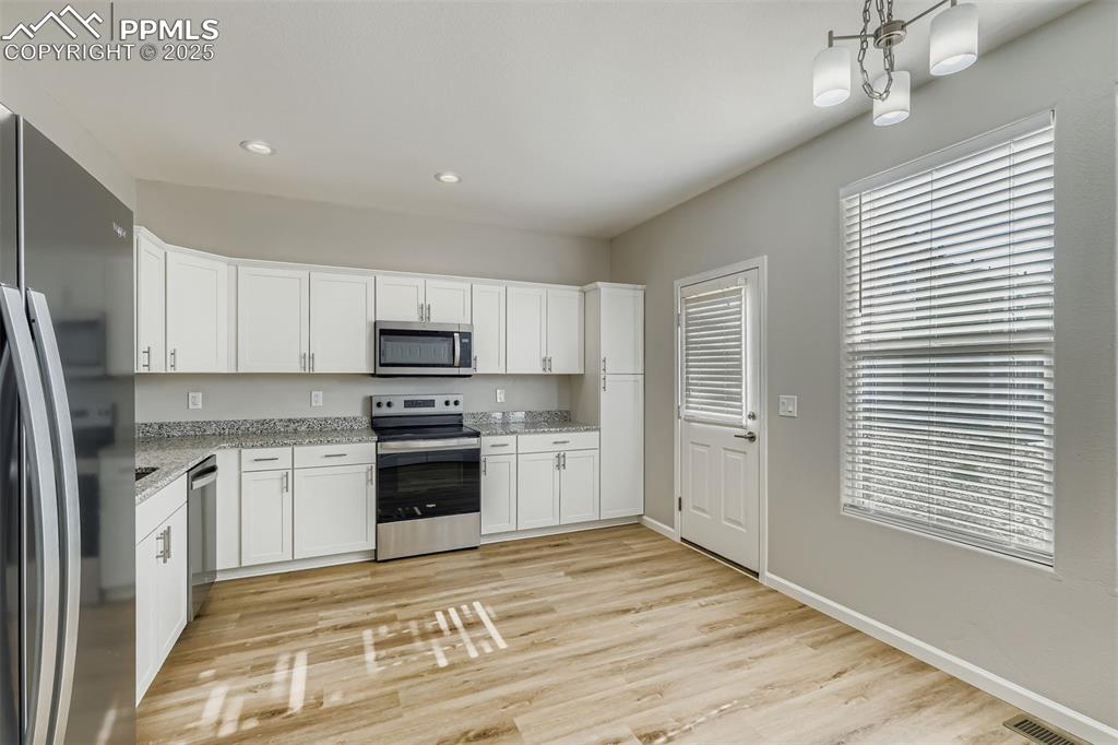 Image 6 of 22: Kitchen with appliances with stainless steel finishes, white cabinets, ligh