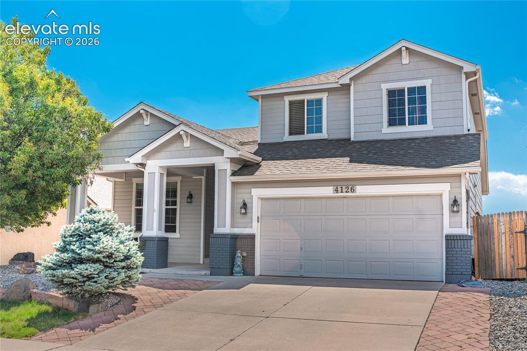 Image 2 of 48: Gray two-story residence featuring a two-car garage, brick paver walkway, a