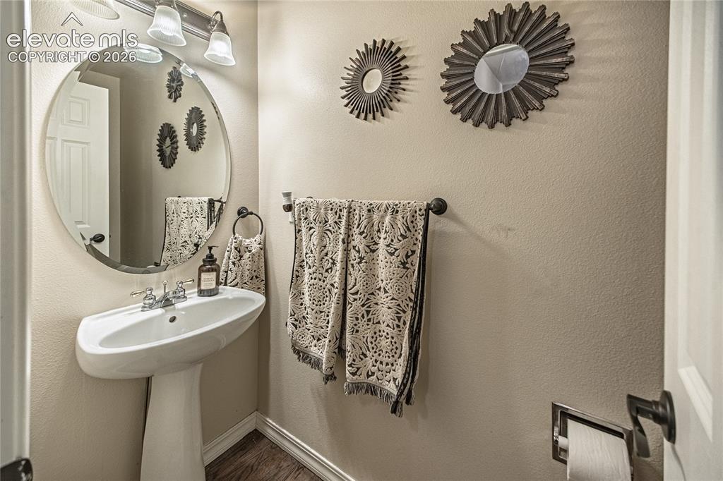 Image 20 of 48: White pedestal sink with chrome faucet, circular mirror, and overhead vanit