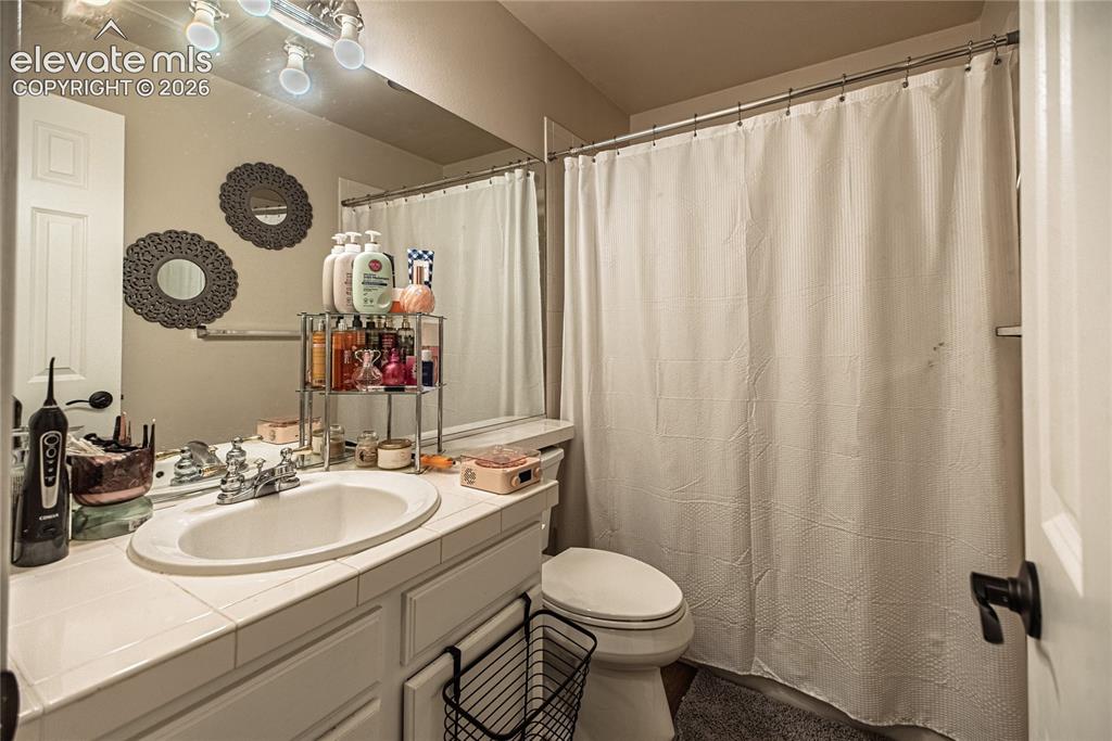 Image 30 of 48: Bathroom featuring a vanity with a drop-in sink, tiled countertop, and a sh