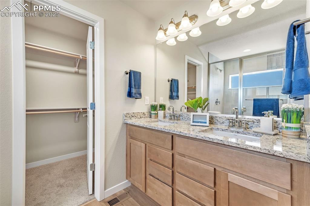 Image 31 of 46: Full bathroom with a walk in closet, a stall shower, and double vanity