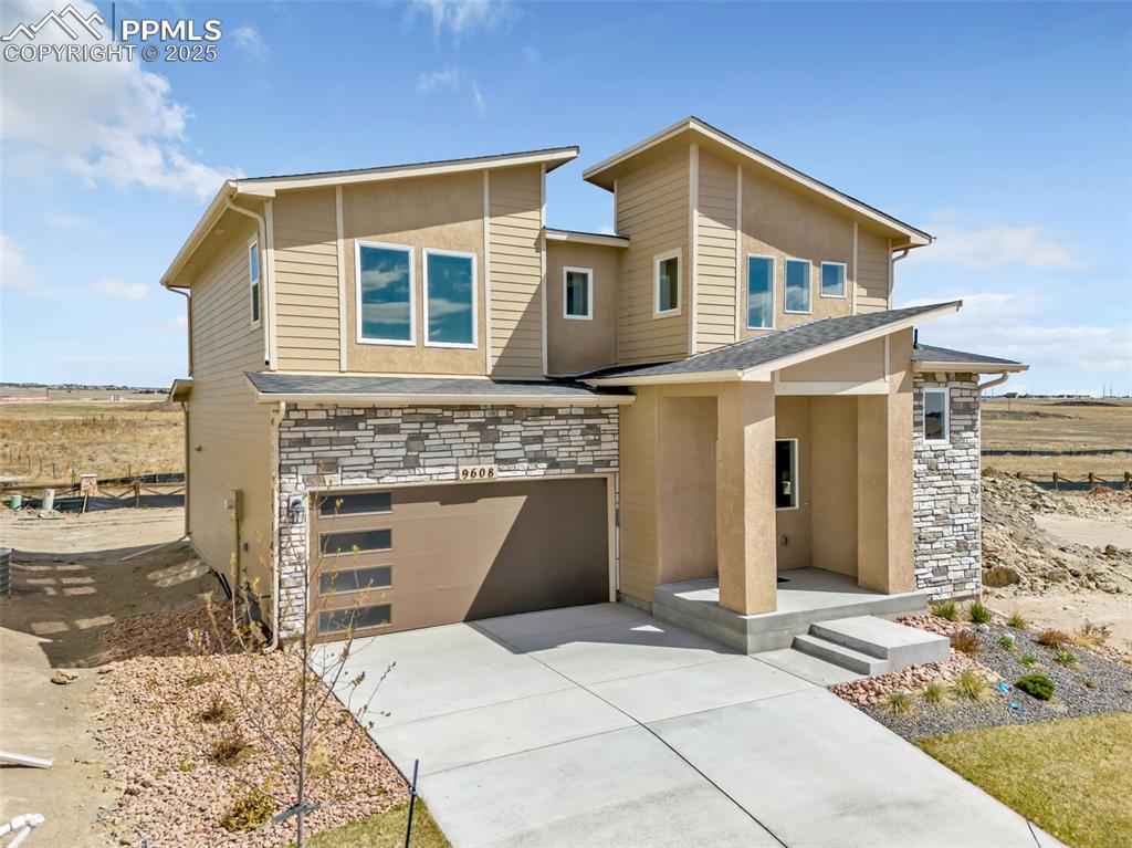 Image 42 of 46: View of front facade with stone siding, concrete driveway, an attached gara