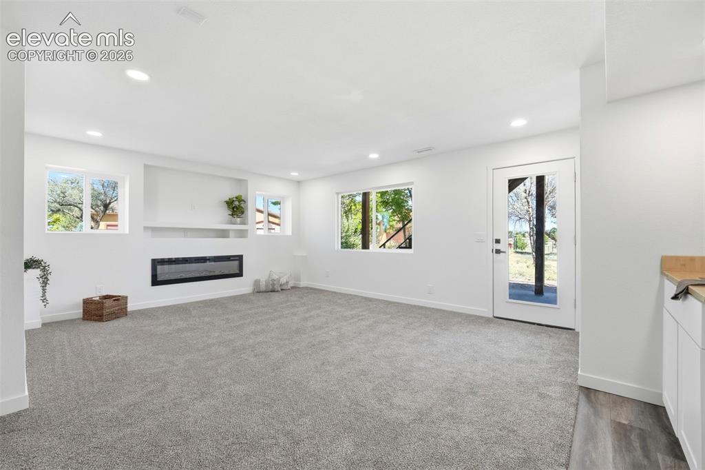 Image 25 of 36: Spacious living area featuring light gray carpeting, a built-in electric fi