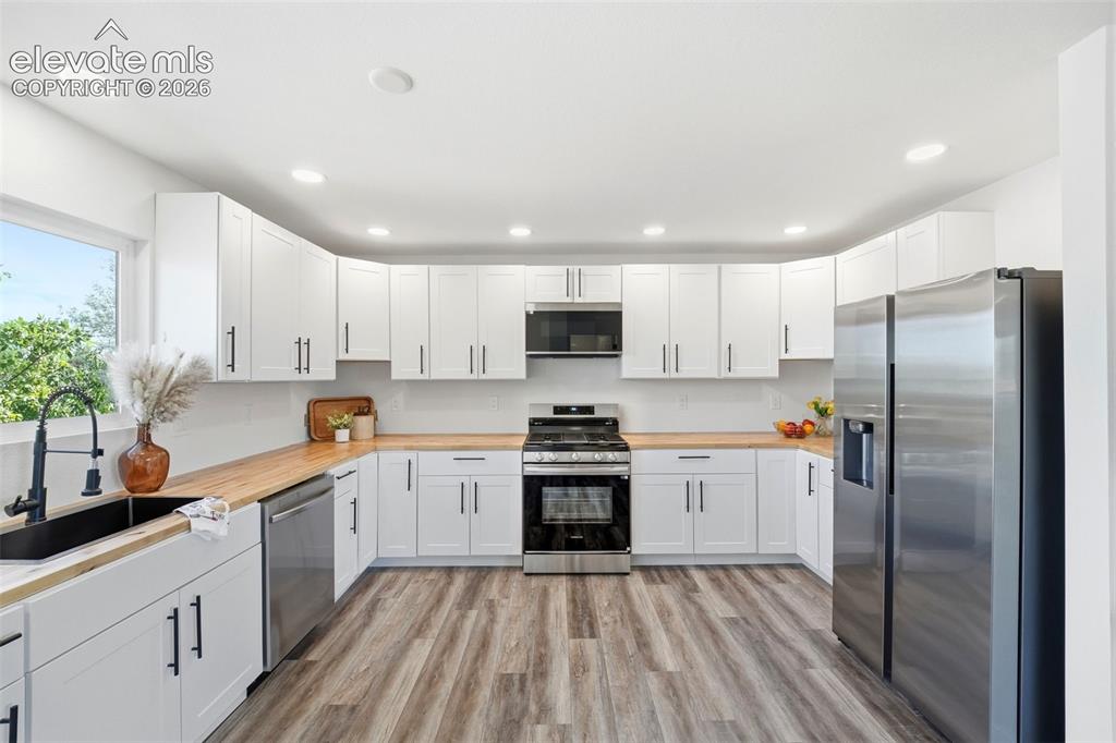 Image 5 of 36: Modern kitchen featuring extensive white cabinetry with matte black hardwar