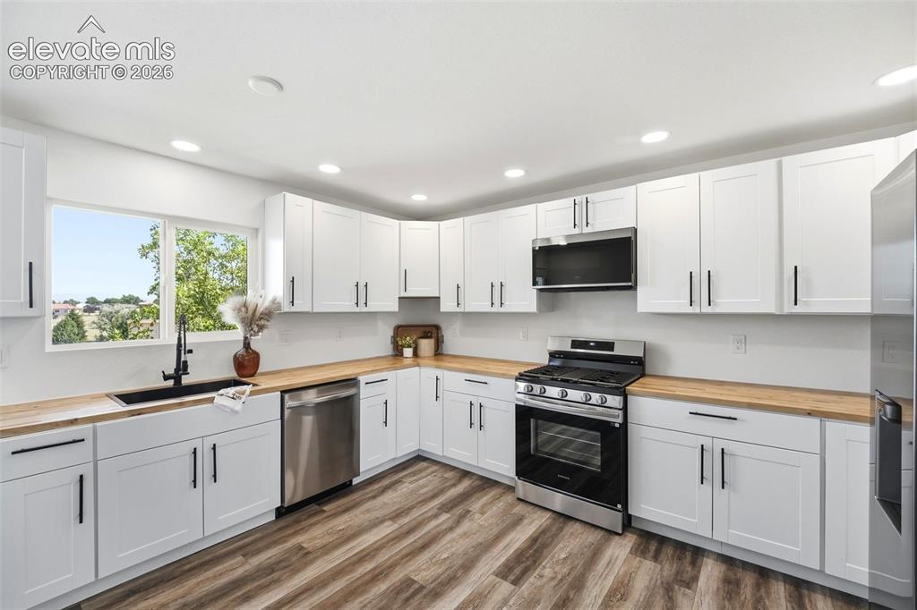 Image 6 of 36: Kitchen featuring white shaker cabinetry with matte black hardware, wood-fi