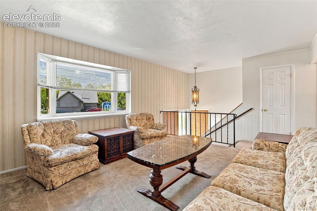 Image 13 of 42: Living area featuring a large bay window, wall-to-wall carpeting, metal sta
