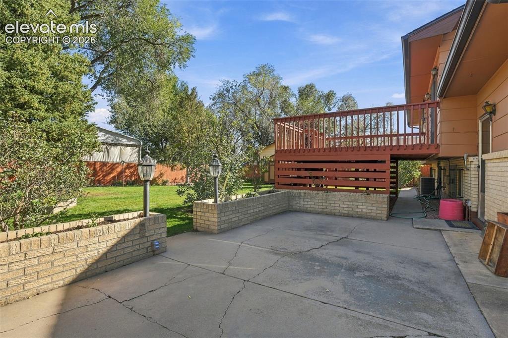 Image 2 of 42: Rear exterior featuring a raised wood deck, paved patio, brick retaining wa